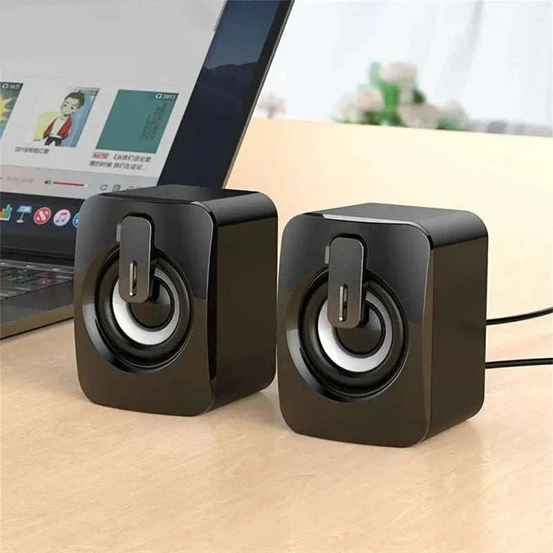 Black USB wired PC computer speakers with LED light on a wooden desk next to a laptop